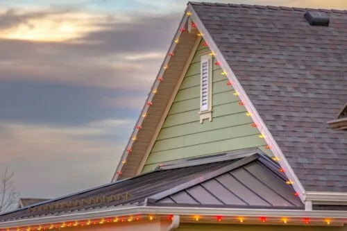 House with Green Siding and a black roof with colorful Christmas Lights.