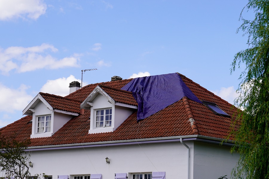 roof experiencing a leak covered with a tarp waiting for the roofing company to fix after spring summer thunderstorm